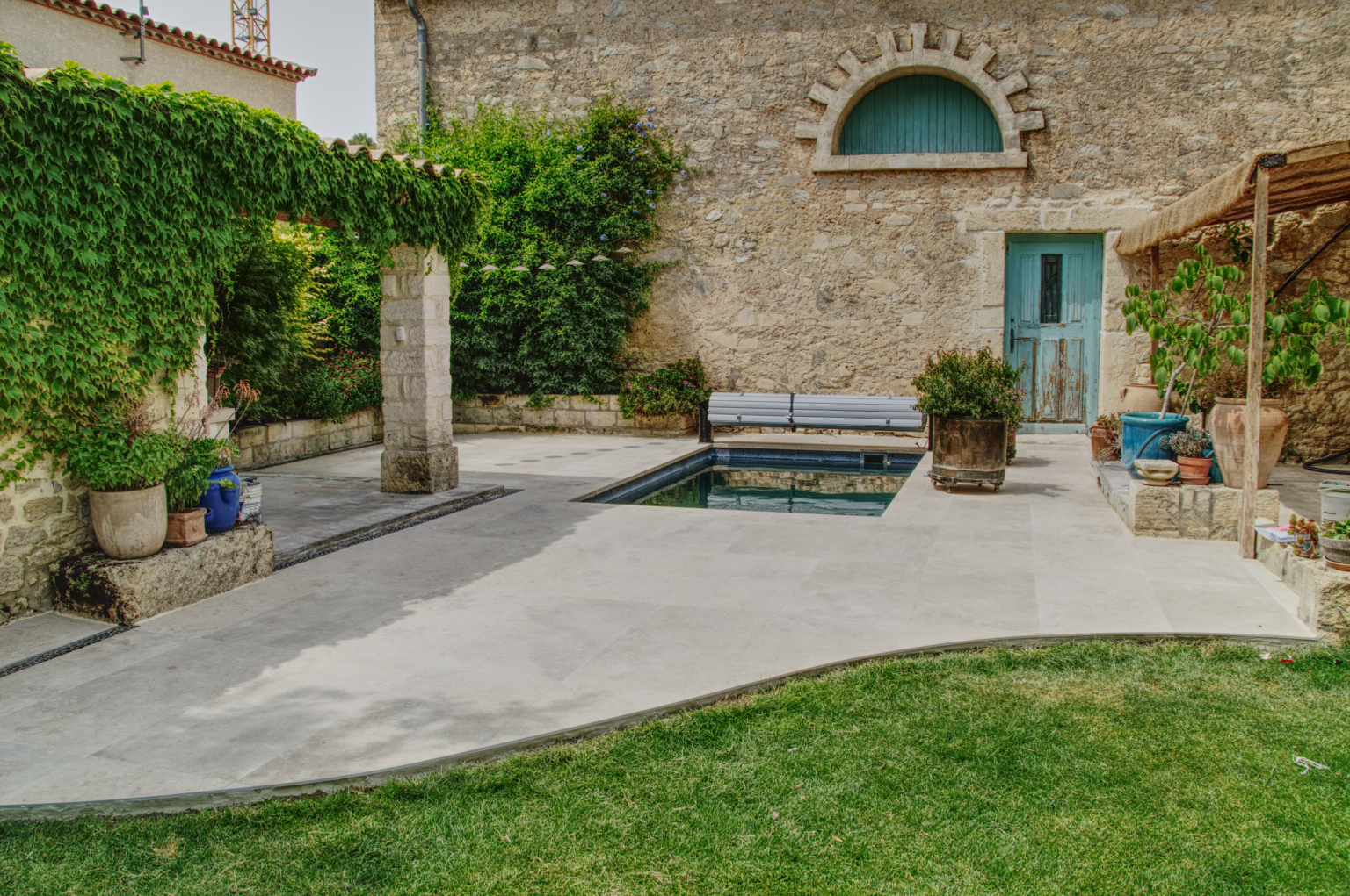 Terrasse en carrelage grand format 120x60 avec découpe courbe sur mesure, posée par CCJ Carrelage à Vendargues. Finition autour d’une piscine et maison en pierre.