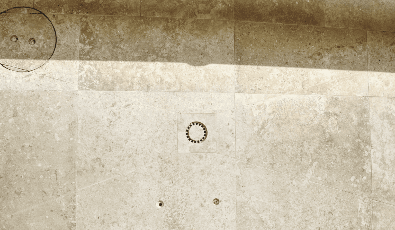 Détail de pose sur mesure autour d’un siphon encastré pour douche extérieure, avec coupes soignées dans des dalles grand format en pierre naturelle. Réalisation par CCJ Carrelage à Vendargues (34), spécialiste en finitions techniques dans les régions de l’Hérault, Gard, Lyon et Provence-Alpes-Côte d’Azur. Un savoir-faire qui combine esthétique et fonctionnalité.