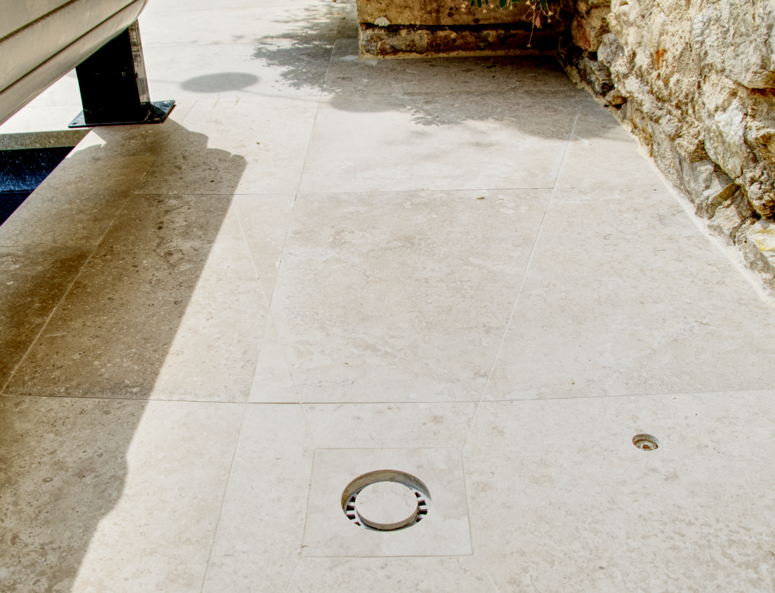 Siphon de douche extérieure intégré dans du carrelage en pierre naturelle, avec découpes précises. Réalisation par CCJ Carrelage à Vendargues, dans l’Hérault.