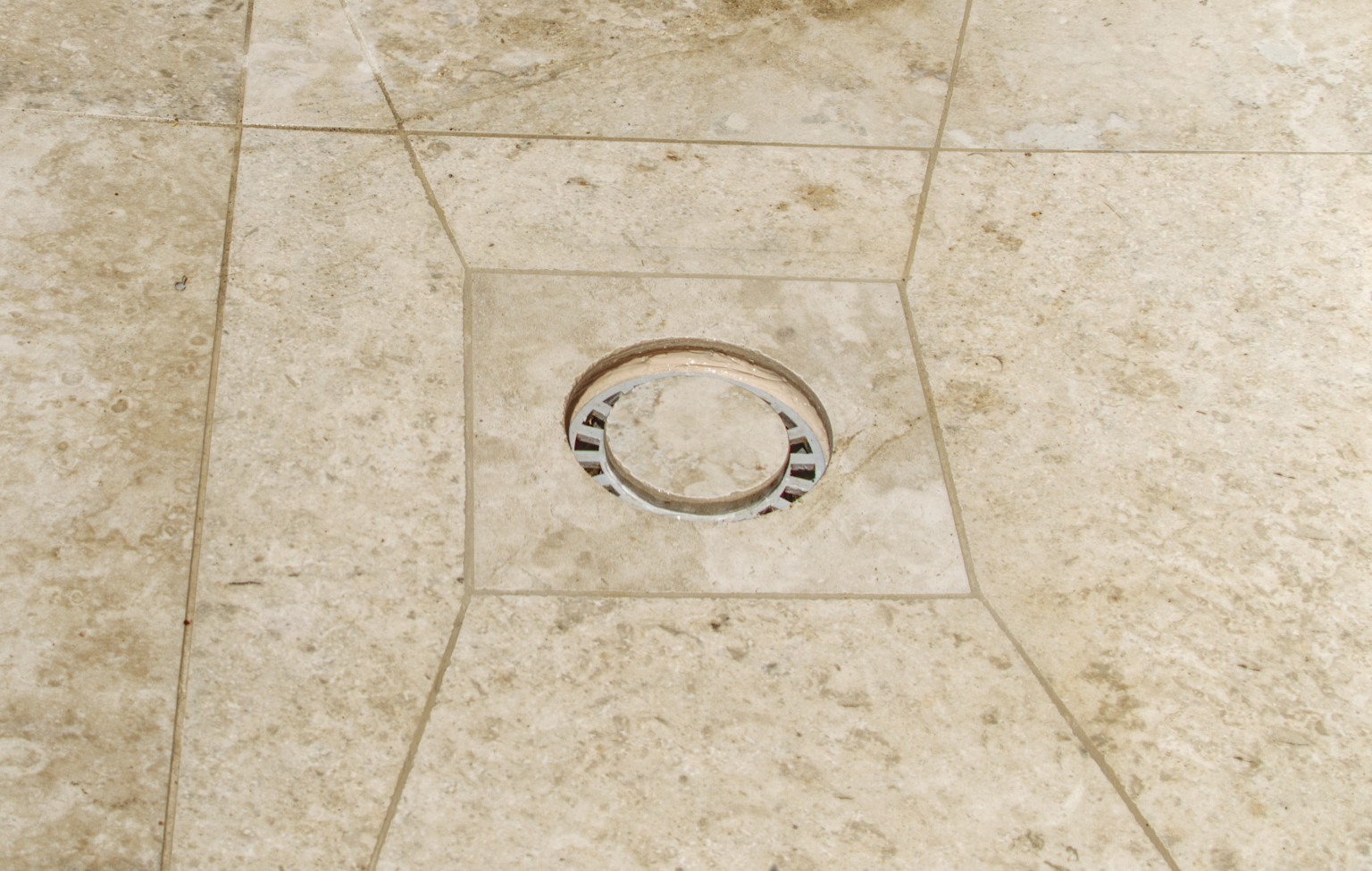 Bonde de douche italienne intégrée avec précision dans un carrelage en travertin. Pose de luxe signée CCJ Carrelage à Vendargues (Hérault).