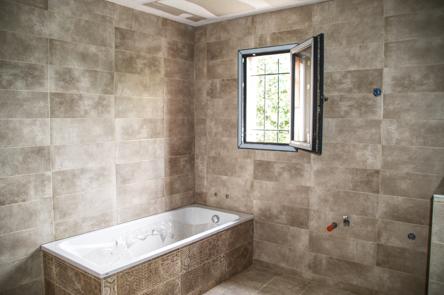 Salle de bain habillée en faïence effet béton avec baignoire encastrée, posée par CCJ Carrelage dans l’Hérault. Finition murale moderne et carrelage décoratif.