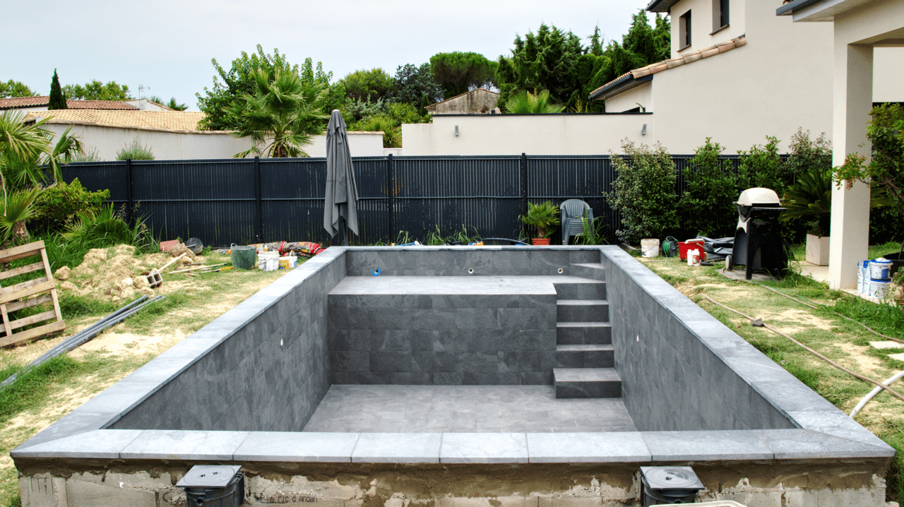 Chantier complet de piscine carrelée en carrelage 30x60 gris effet pierre, réalisé par CCJ Carrelage à Montpellier (Hérault). Escalier intégré, banquette et margelles.