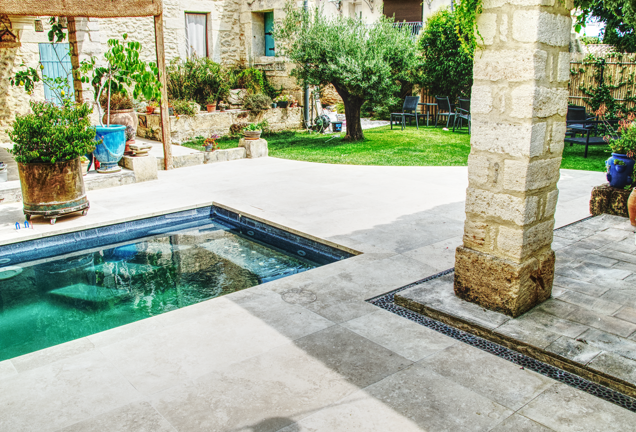 Terrasse carrelée en dalles grand format autour d’une piscine, posée devant une maison en pierre à Vendargues. Finitions soignées avec grilles d’évacuation discrètes.